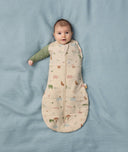 Baby lies on a soft blue blanket, dressed in a Cocoon Swaddle Bag with its one arm outside.