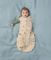 Baby lies on a soft blue blanket, dressed in a Cocoon Swaddle Bag with its one arm outside.