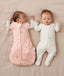 Two babies lying on their backs, one wearing an ergoPouch Cocoon Swaddle Bag 2.5 TOG Dasies with arm out sleeping, and the other in a Long Sleeve Layer Oatmeal Marle