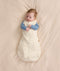 Baby lying on a cream-colored fabric background wearing a Cocoon Swaddle Bag with a blue Long Sleeve Layer underneath.