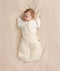 Newborn baby wearing a cream patterned Cocoon Swaddle Bag with Butterfly Cardi layered over top for hands up sleeping.