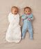 Two babies lying on their backs, one wearing an ergoPouch Cocoon Swaddle Bag 2.5 TOG Oatmeal Marle with arm in sleeping, and the other in a Long Sleeve Layer Dragonflies