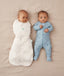 Two babies lying on their backs, one wearing an ergoPouch Cocoon Swaddle Bag 2.5 TOG Oatmeal Marle with arm in sleeping, and the other in a Long Sleeve Layer Dragonflies