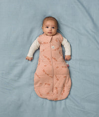 Baby lies on a soft blue blanket, wearing an ergoPouch Cocoon Swaddle Bag with its arms outside.