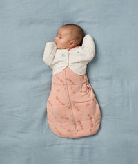 Baby is sleeping on a soft blue blanket, wearing a Butterfly Cardi over a Cocoon Swaddle Bag.
