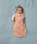 Baby lies on a soft blue blanket, wearing an ergoPouch Cocoon Swaddle Bag with its one arm outside.