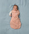 Baby lies on a soft blue blanket, wearing an ergoPouch Cocoon Swaddle Bag with its one arm outside.