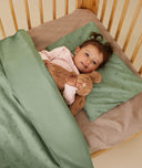 Toddler cuddling a teddy lying on top of a ergoPouch Organic Toddler Pillow Case Willow