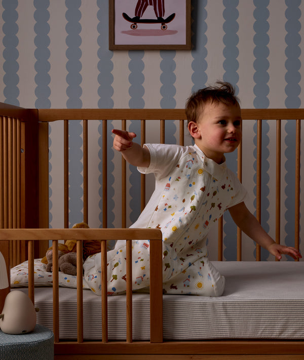 Child sitting on his bed with a Organic Toddler Pillow and Case Daydream, wearing a Sleep Suit Bag 1.0 TOG Daydream.