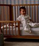 Child sitting in a wooden crib with Organic Toddler Pillow and Case Daydream, wearing a Sleep Suit Bag 1.0 TOG Daydream.