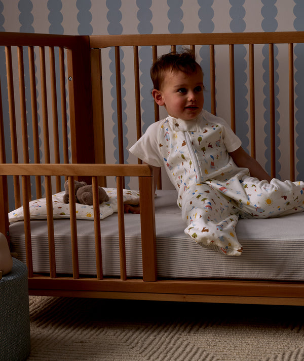 Child sitting in a wooden crib with Organic Toddler Pillow and Case Daydream, wearing a Sleep Suit Bag 1.0 TOG Daydream.