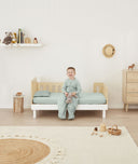 Toddler sitting on the side of a bed made with ergoPouch Organic Fitted Sheet Sage