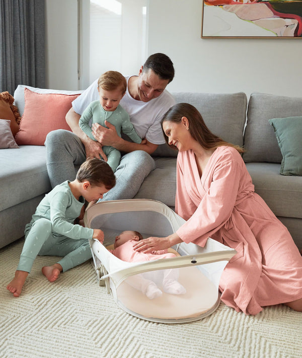 Family gathering around infant resting in ergoPouch Easy Sleep Portable Crib Ecru