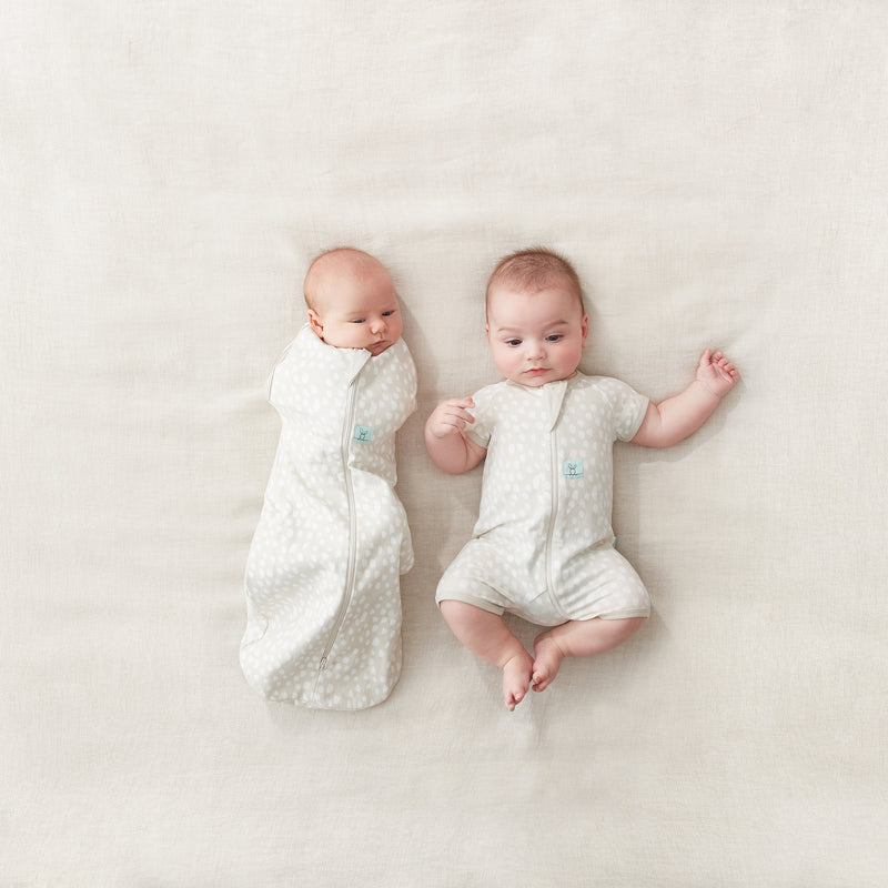 Two babies lying side by side. One wearing a Cocoon Swaddle Bag, while the other is wearing a short sleeve layer