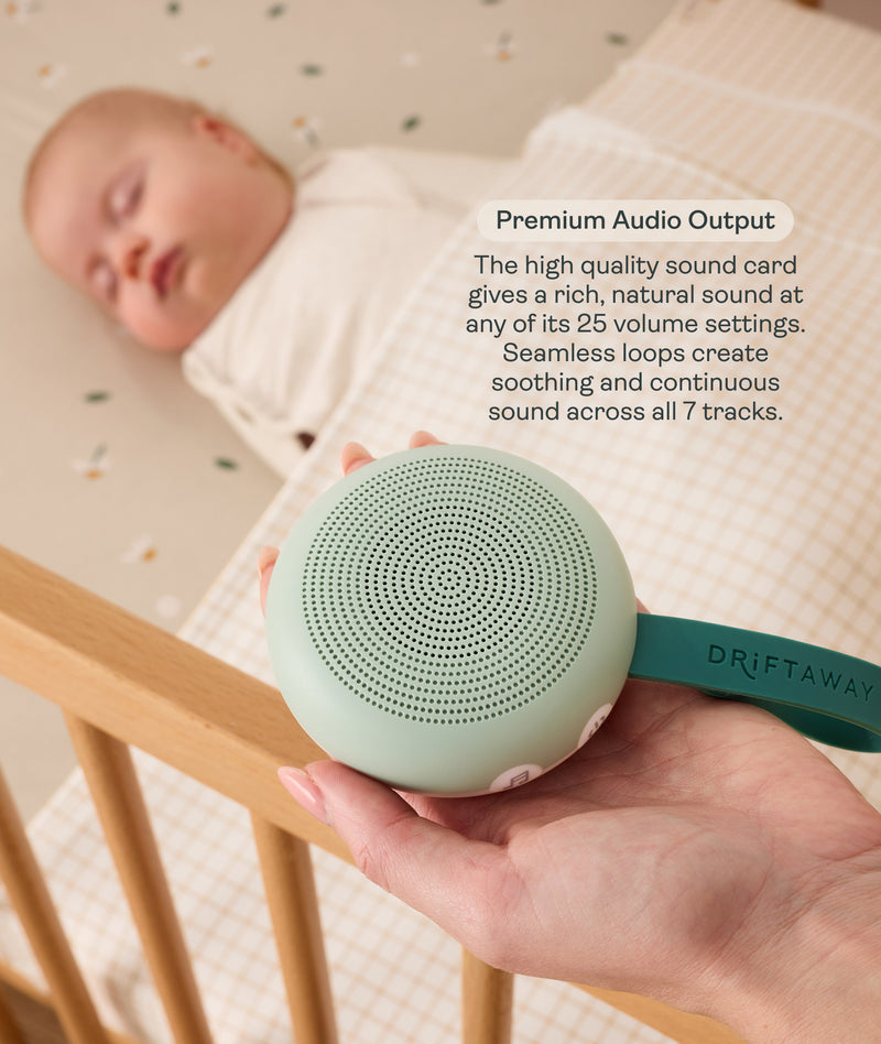An adult hand holds a round, mint-green Drift Away white noise machine next to a cot where a baby is peacefully sleeping. A text box highlights 