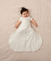 Baby lying in ergoPouch Hip Harness Jersey Sleep Bag 0.2 TOG Oatmeal Marle and smiling to the camera 