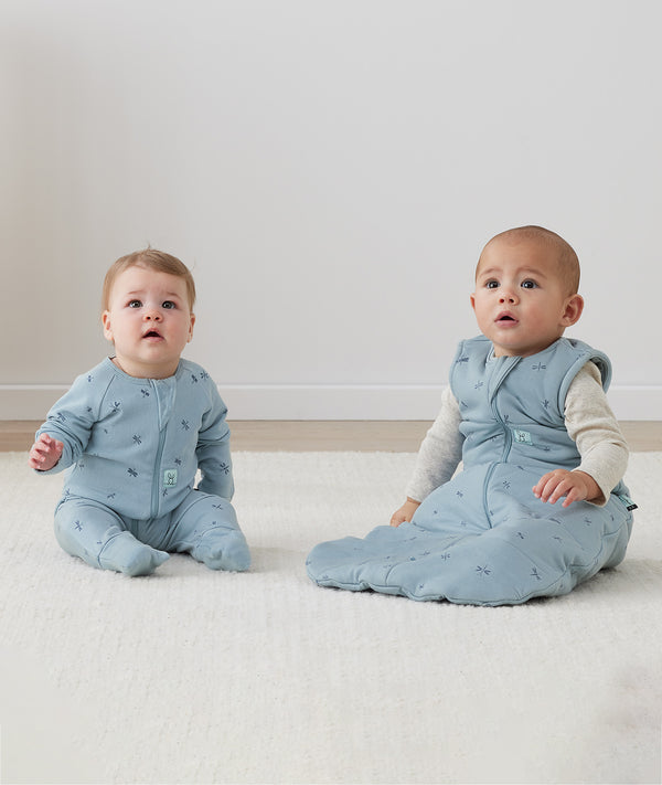 Two infants sitting on the floor both wearing ergPouch Dragonflies, one in a Long Sleeve Layer 1.0 TOG and the other in a Sleeping Bag 2.5 TOG, perfect layering for the colder months