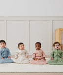 Four babies sitting on a white floor wearing ergoPouch Sleeping Bag Sleeved in 2.5 and 3.5 TOGs in heritage colours: Dragonflies, Oatmeal Marle, Daisies and Willow.