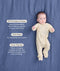 Baby lying on a blue blanket wearing a cream patterned Long Sleeve Layer with text highlighting GOTS Organic Cotton, TOG Ratings, and Three-way zipper.