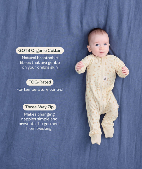 Baby lying on a blue blanket wearing a cream patterned Long Sleeve Layer with text highlighting GOTS Organic Cotton, TOG Ratings, and Three-way zipper.