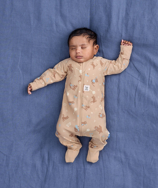 Sleeping baby lying on a blue fabric background wearing a beige patterned Long Sleeve Layer with fold-over cuffs