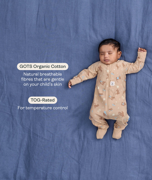 Sleeping baby in a tan patterned Long Sleeve Layer on a blue fabric background, with text highlighting GOTS Organic Cotton and TOG-Rated features.