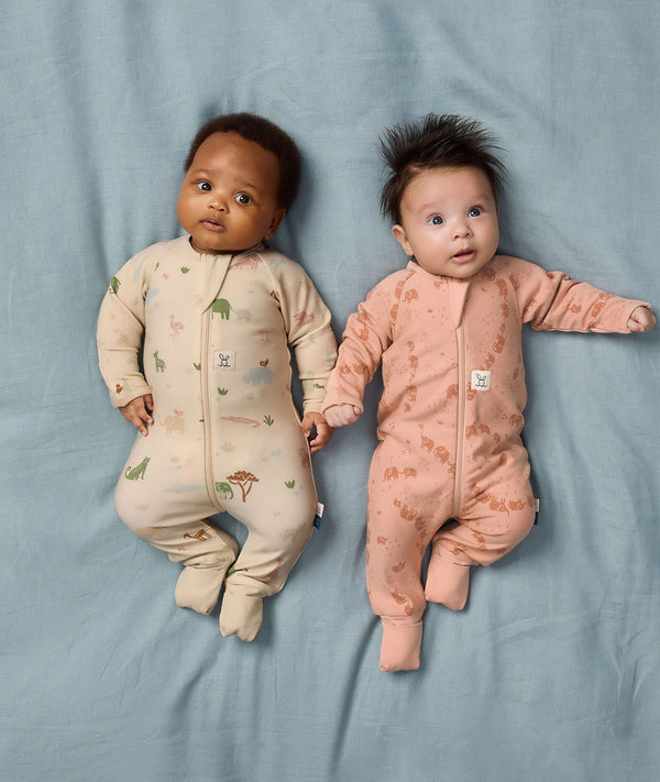 Two babies lying side by side wearing ergoPouch Long Sleeve Layers 1.0 TOG in Savannah and Elephant Parade