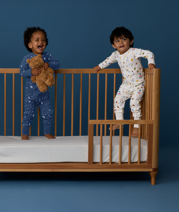 Two children standing in a crib wearing ergoPouch Long Sleeve Layer 1.0 TOG Daydream and Starbeam