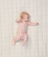 Baby lying on a checkered blanket, dressed in an ergoPouch Long Sleeve Layer with its foot cuffs folded over for extra warmth and protection.