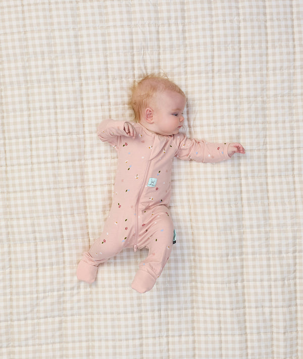 Baby lying on a checkered blanket, dressed in an ergoPouch Long Sleeve Layer with its foot cuffs folded over for extra warmth and protection.