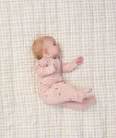 Baby lying on a beige checkered blanket, wearing a light pink long sleeve layer with small floral prints.