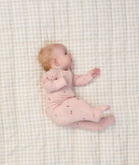 Baby lying on a beige checkered blanket, wearing a light pink long sleeve layer with small floral prints.