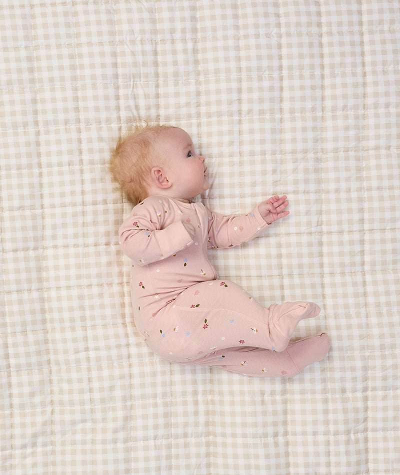 Baby lying on a beige checkered blanket, wearing a light pink long sleeve layer with small floral prints.