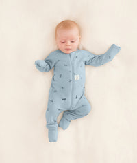 Baby is lying on a neutral coloured blanket, wearing a blue Long Sleeve Layer with its hand and foot cuffs folded over.