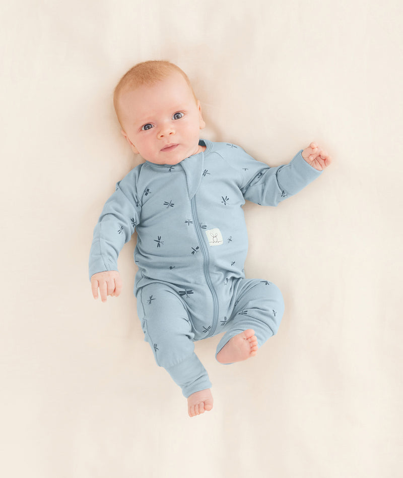 Baby is lying on a neutral coloured blanket, wearing a blue Long Sleeve Layer with dragonfly prints.
