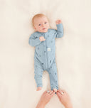 A parent is dressing their baby in a blue long-sleeve layer, carefully folding the foot cuffs.