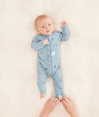 A parent is dressing their baby in a blue long-sleeve layer, carefully folding the foot cuffs.