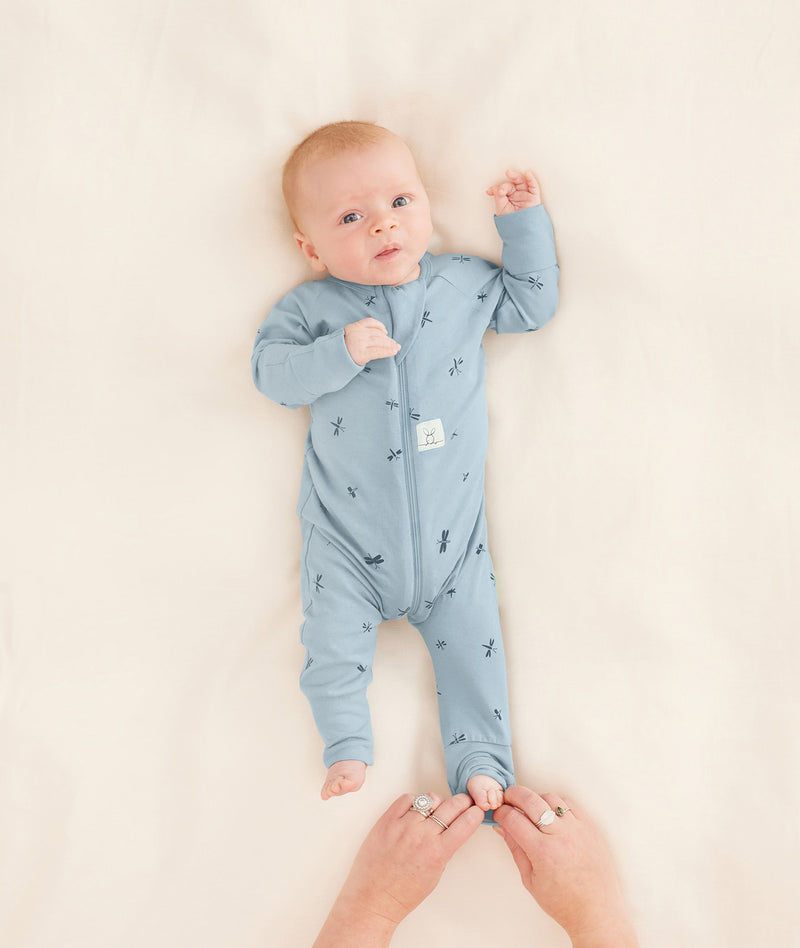 A parent is dressing their baby in a blue long-sleeve layer, carefully folding the foot cuffs.