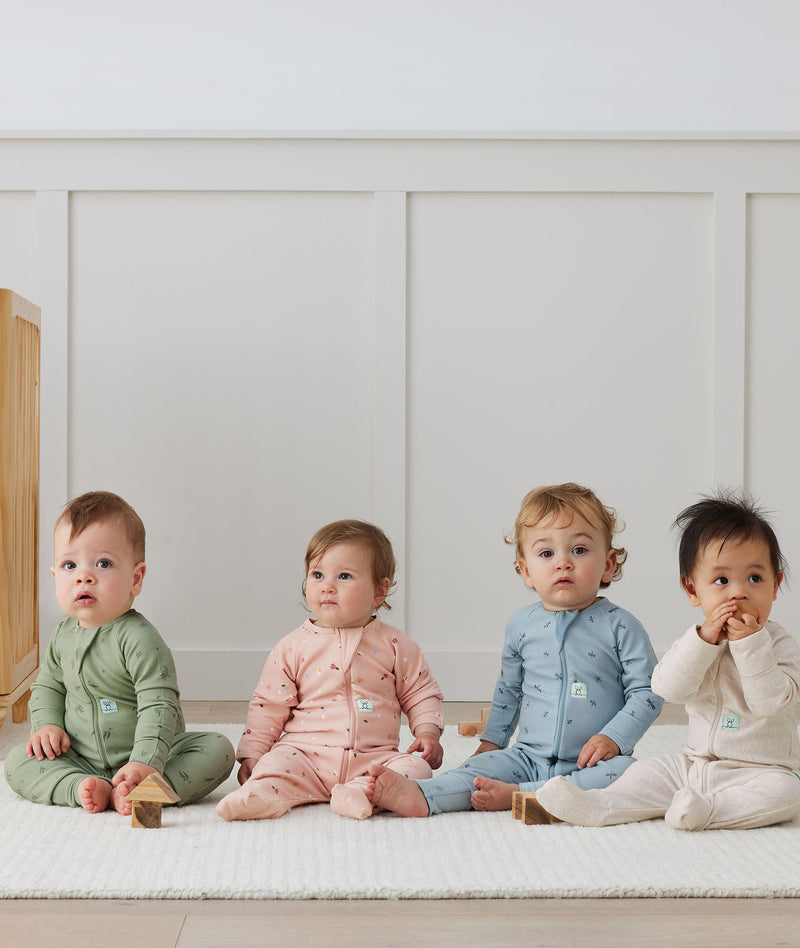 Four infants are seated side by side, each wearing ergPouch Long Sleeve Layers in the colors of Willow, Daisies, Dragonflies, and Oatmeal Marle.