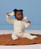 Baby sitting on a quilted brown mat against a light blue background, wearing a cream patterned Long Sleeve Layer, holding a wooden maraca in each hand.