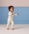 Toddler walking indoors wearing a cream, subtly patterned Long Sleeve Layer against a blue wall background.
