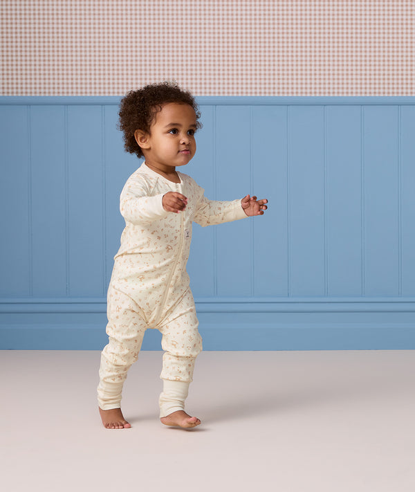 Toddler walking indoors wearing a cream, subtly patterned Long Sleeve Layer against a blue wall background.