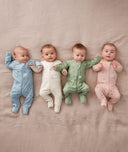 Four babies are lying on a soft pink blanket, each wearing ergPouch Long Sleeve Layers in the colors of Dragonflies, Oatmeal Marle, Willow, and Daisies.