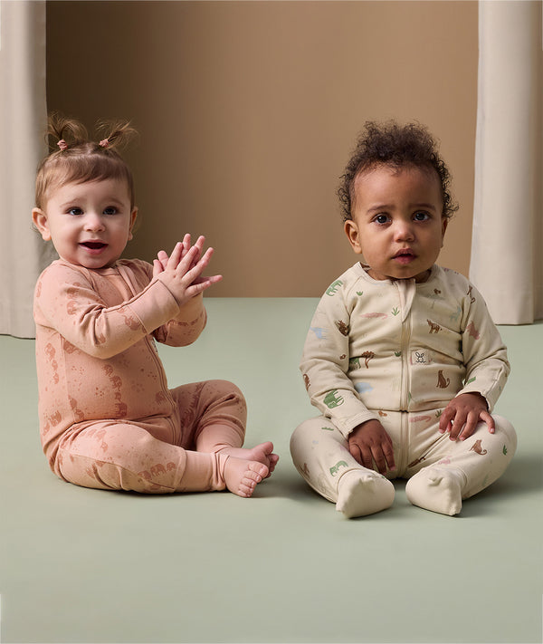 Two infants sitting on a floor wearing an ergoPouch Long Sleeve Layer in Elephant Parade and Savannah