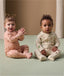 Two infants sitting on a floor wearing an ergoPouch Long Sleeve Layer in Elephant Parade and Savannah