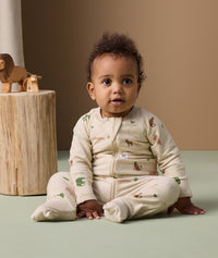 Infant sitting on the floor in ergoPouch Long Sleeve Layer 1.0 TOG Savannah with foot cuffs folded over.