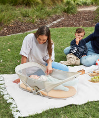Woman sitting on a blanket outdoors with a child in an ergoPouch Easy Sleep Portable Crib