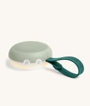 Portable white noise machine with a soft green silicone exterior, white control buttons, a built-in night light at the base, and a flexible dark green loop handle for hanging or carrying.