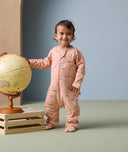 A toddler stands beside a globe, wearing an ergoPouch Sleep Onesie 2.5 TOG in Elephant Parade.