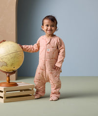 A toddler stands beside a globe, wearing an ergoPouch Sleep Onesie 2.5 TOG in Elephant Parade.